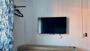 A room with a flat-screen TV mounted on the wall, a wooden dresser, and a patterned curtain.