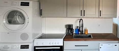 A compact kitchen with a washing machine, oven, dishwasher, and a sink with a faucet.