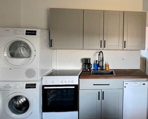 Eine kompakte Küche mit Waschmaschine, Backofen, Geschirrspüler und Spüle mit Armatur.