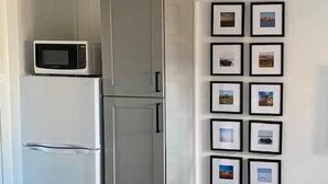 A kitchen with a white refrigerator, a microwave, and a dishwasher. There are framed pictures on the wall.