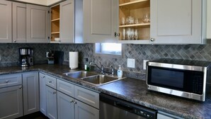 A modern kitchen with grey cabinets, a stainless steel dishwasher, a coffee maker, a microwave, and a window above the sink.