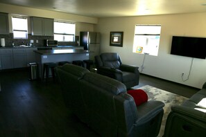 Sala de estar com sofá, televisão e cozinha ao fundo.