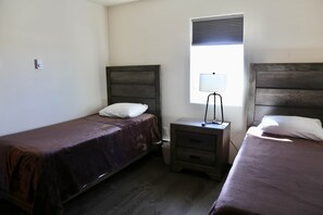 Una habitación con dos camas individuales, una mesita de noche con lámpara y una ventana con persianas.