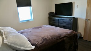 A bedroom with a bed, a dresser, a television, and a window.