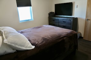 Un dormitorio con cama, cómoda, televisor y ventana.