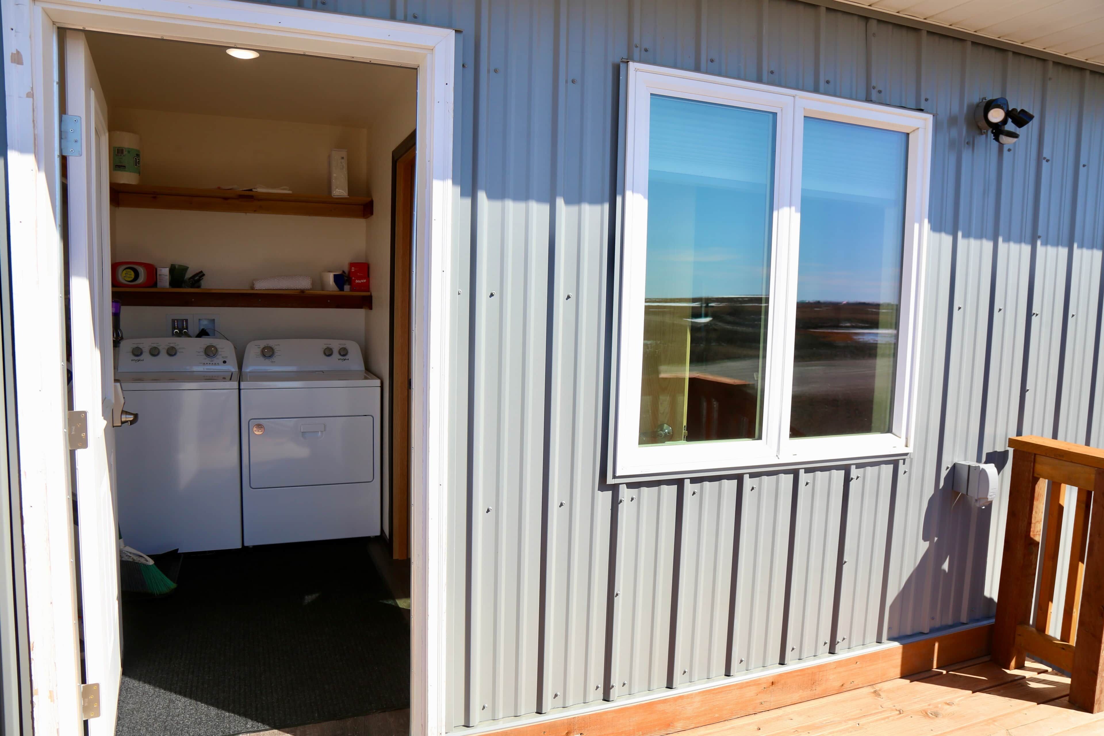 A laundry room with two washing machines, a window, and a wooden deck.