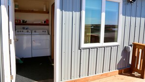 A laundry room with two washing machines, a window, and a wooden deck.