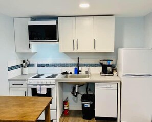A compact kitchen with white cabinets, a stove, a sink, and a refrigerator.
