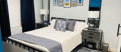 A hotel room with a bed, bedside table, lamp, and a rug.