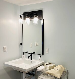 A bathroom with a white sink, black faucet, and a mirror with three lights. There are towels and a hairdryer on the counter.