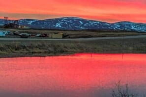 Ein Gewässer spiegelt einen Sonnenuntergang mit schneebedeckten Bergen im Hintergrund.