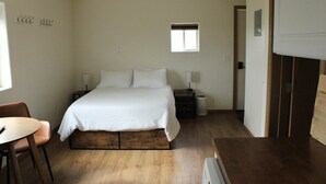 Een slaapkamer met een bed, nachtkastjes, een stoel, een klein raam en een deur.