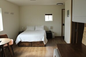 Ein Schlafzimmer mit einem Bett, Nachttischen, einem Sessel, einem kleinen Fenster und einer Tür.