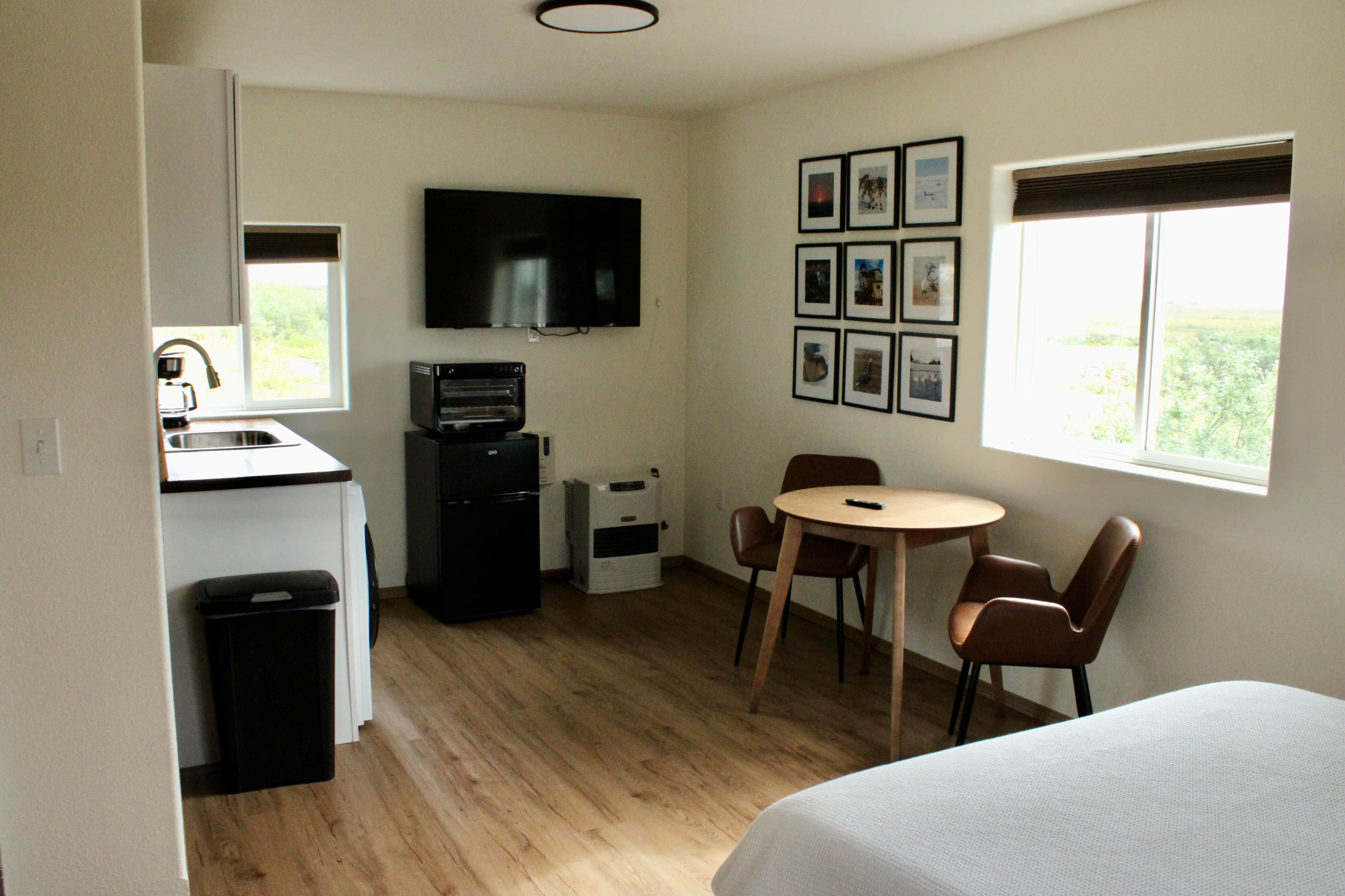 Une pièce compacte comprenant un coin cuisine, un espace repas avec une table et des chaises, un lit et un téléviseur fixé au mur.
