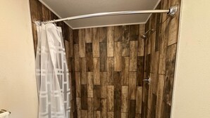 Een douche met een wand van houten panelen, een wit bad en een douchegordijn.