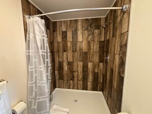 Eine Dusche mit Holzwand, einer weißen Badewanne und einer Duschvorhang.