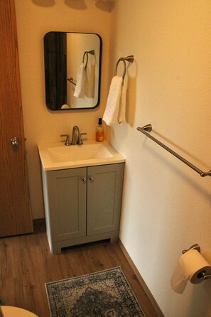 A bathroom with a sink, mirror, towel rack, and a toilet paper holder.
