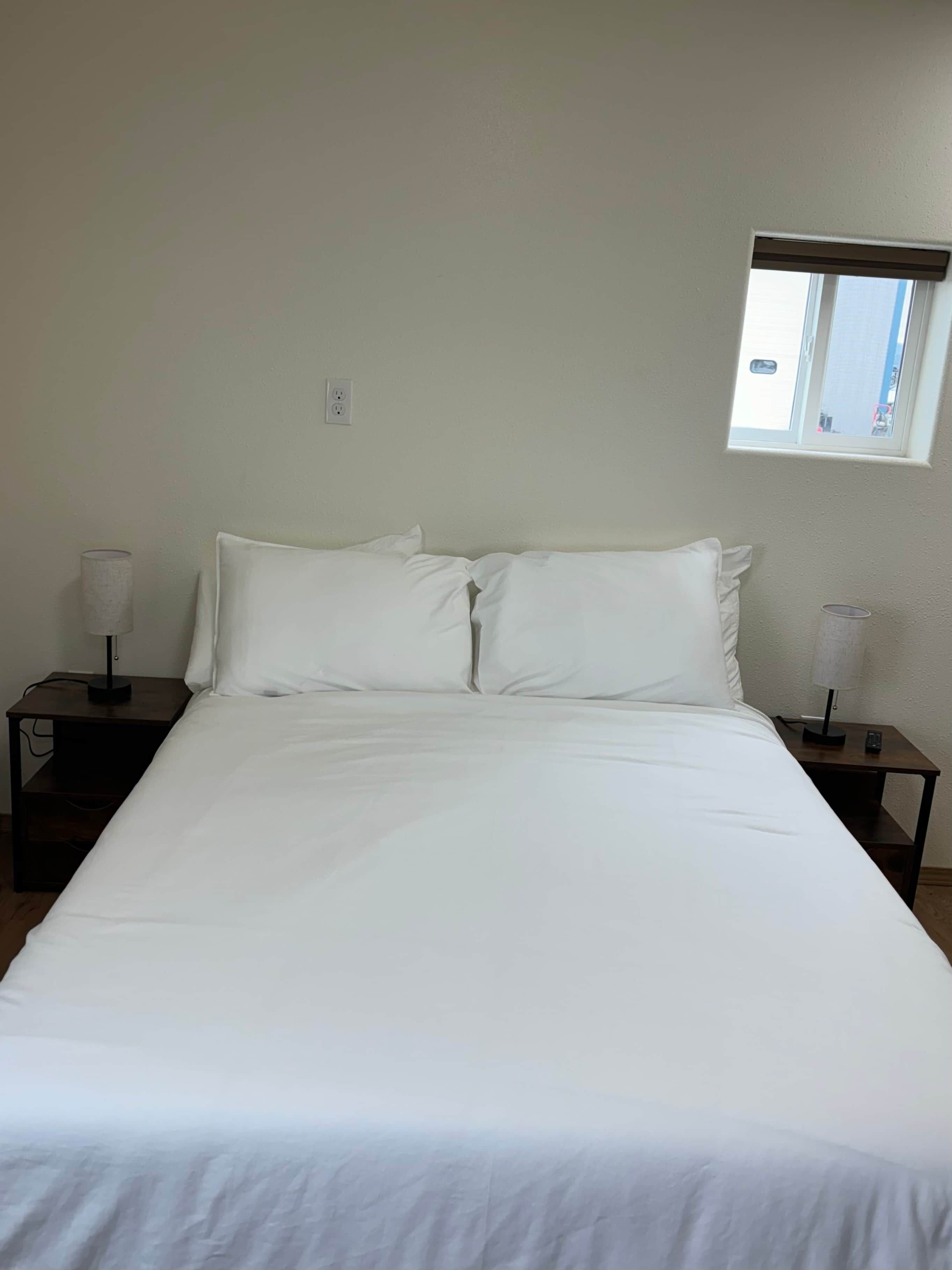 Ein Standardhotelzimmer mit einem großen Bett, zwei Nachttischen, einem Fenster und einer Steckdose.