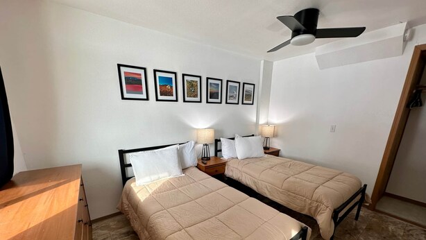 A room with two beds, a ceiling fan, and a series of framed pictures on the wall. - Sockeye Suite at Noxapaga Suites (Nome)
