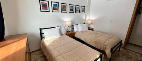 A room with two beds, a ceiling fan, and a series of framed pictures on the wall.
