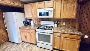A compact kitchen with wooden cabinets, a white refrigerator, a microwave, a gas stove, and a sink. - Sockeye Suite at Noxapaga Suites (Nome)
