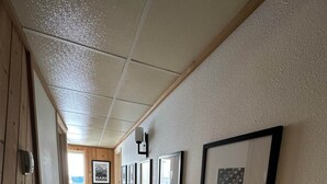 A hallway with framed pictures on the wall, wooden paneling on one side, and a tiled floor. - Sockeye Suite at Noxapaga Suites (Nome)