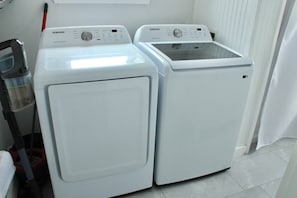 Two white Samsung front-loading washing machines in a laundry room with a red mop and a white towel rack.