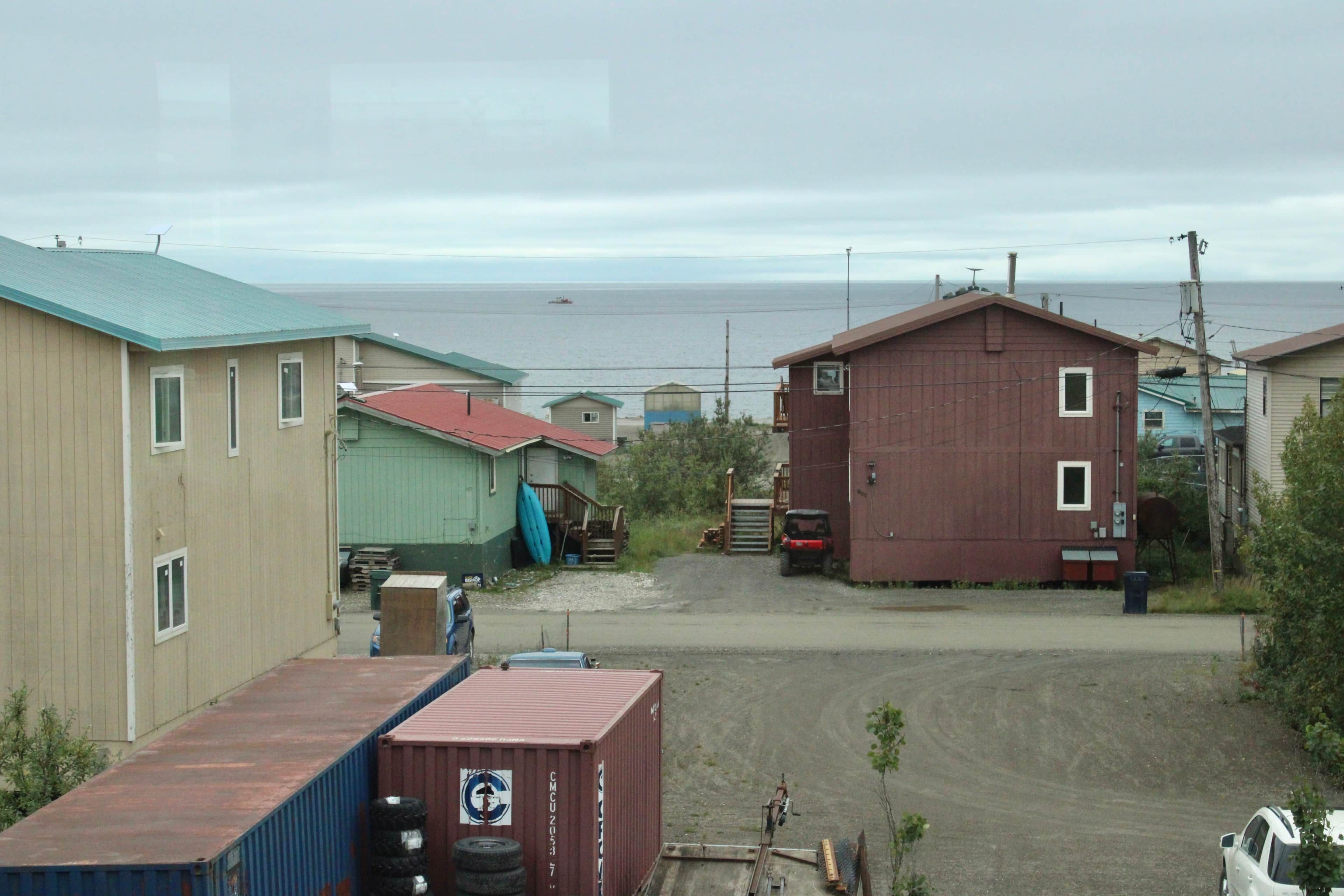 Un barrio costero con casas, un camino de tierra y vista al mar.