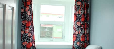 A small bedroom with a single bed, a window with curtains, and a door.