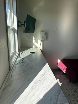 A room with a television mounted on the wall, a power outlet, and a window. - Eureka Suite at Noxapaga Suites (Nome)