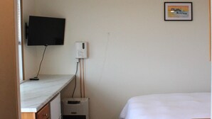 Quarto com cama, escrivaninha com computador, televisão e aquecedor pequeno.