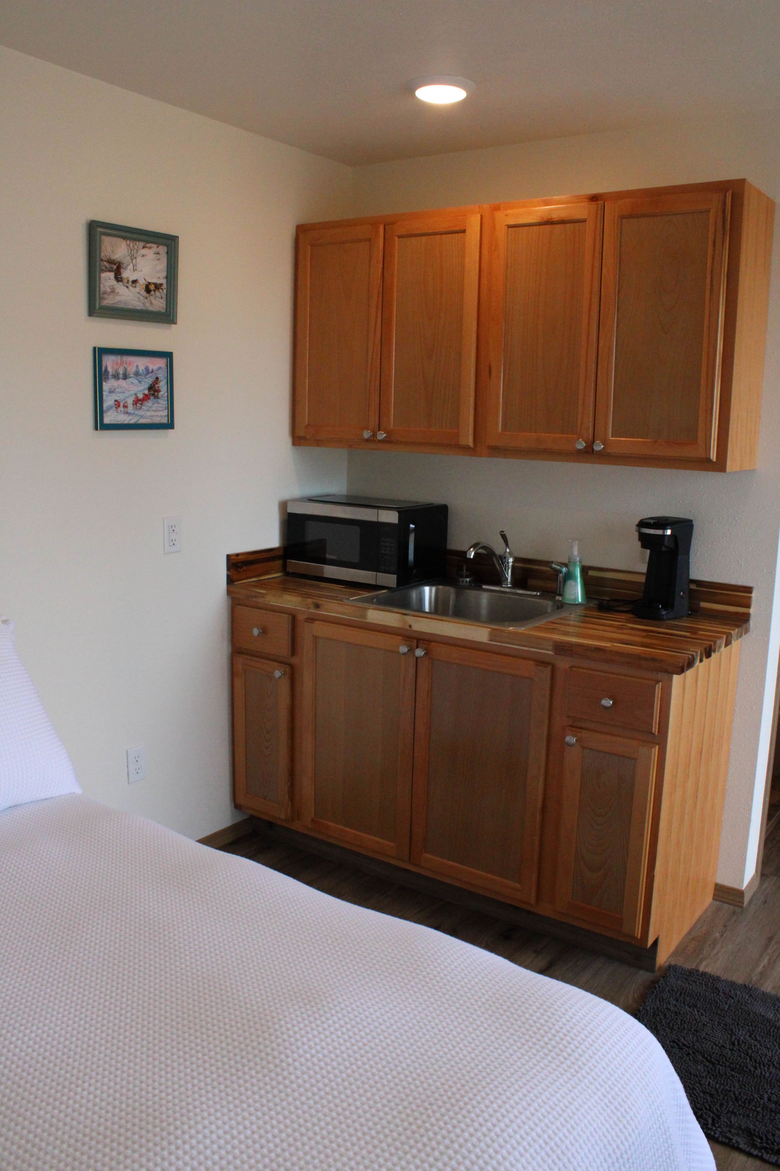 A compact kitchen with wooden cabinets, a microwave, a sink, and a coffee maker.
