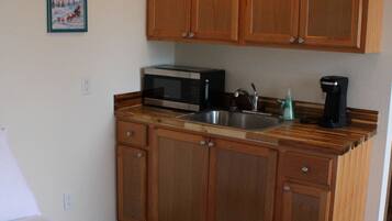 A compact kitchen with wooden cabinets, a microwave, a sink, and a coffee maker.