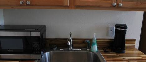 A kitchen with wooden cabinets, a stainless steel sink, a microwave, a coffee maker, and a bottle of dish soap.