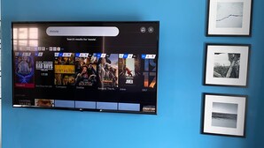 En platt-TV som är monterad på en blå vägg och visar ett gränssnitt för filmströmning med olika filmalternativ.