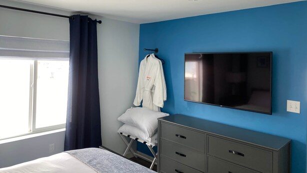 Ett hotellrum med en säng, en tv, en byrå och ett fönster med gardiner.