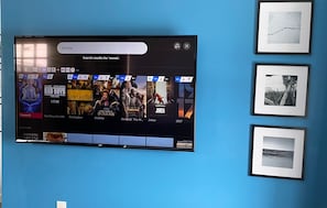 Televisor de pantalla plana fixat a una paret blava que mostra una interfície de reproducció de pel·lícules amb diverses opcions.