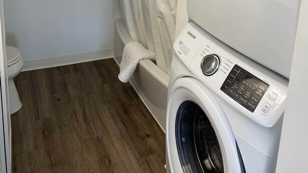 A laundry room with stacked washers and dryers, a shower curtain, and a wooden floor. - Trout Suite at Noxapaga Suites (Nome)