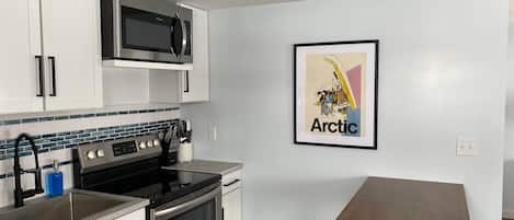 A modern kitchen with stainless steel appliances, a tiled backsplash, and a framed picture on the wall.