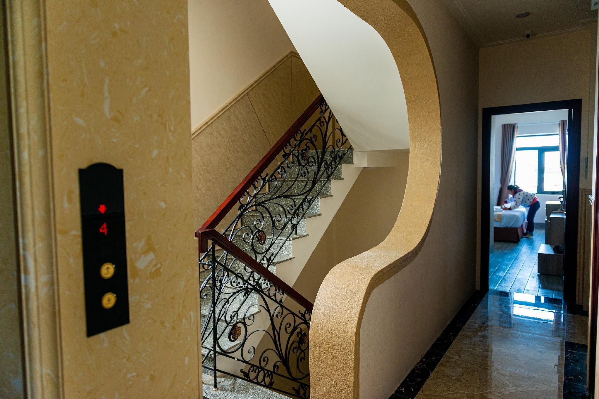 Corredor de hotel com parede curva, escada com grades de metal ornamentadas e um quarto visível por uma porta aberta.