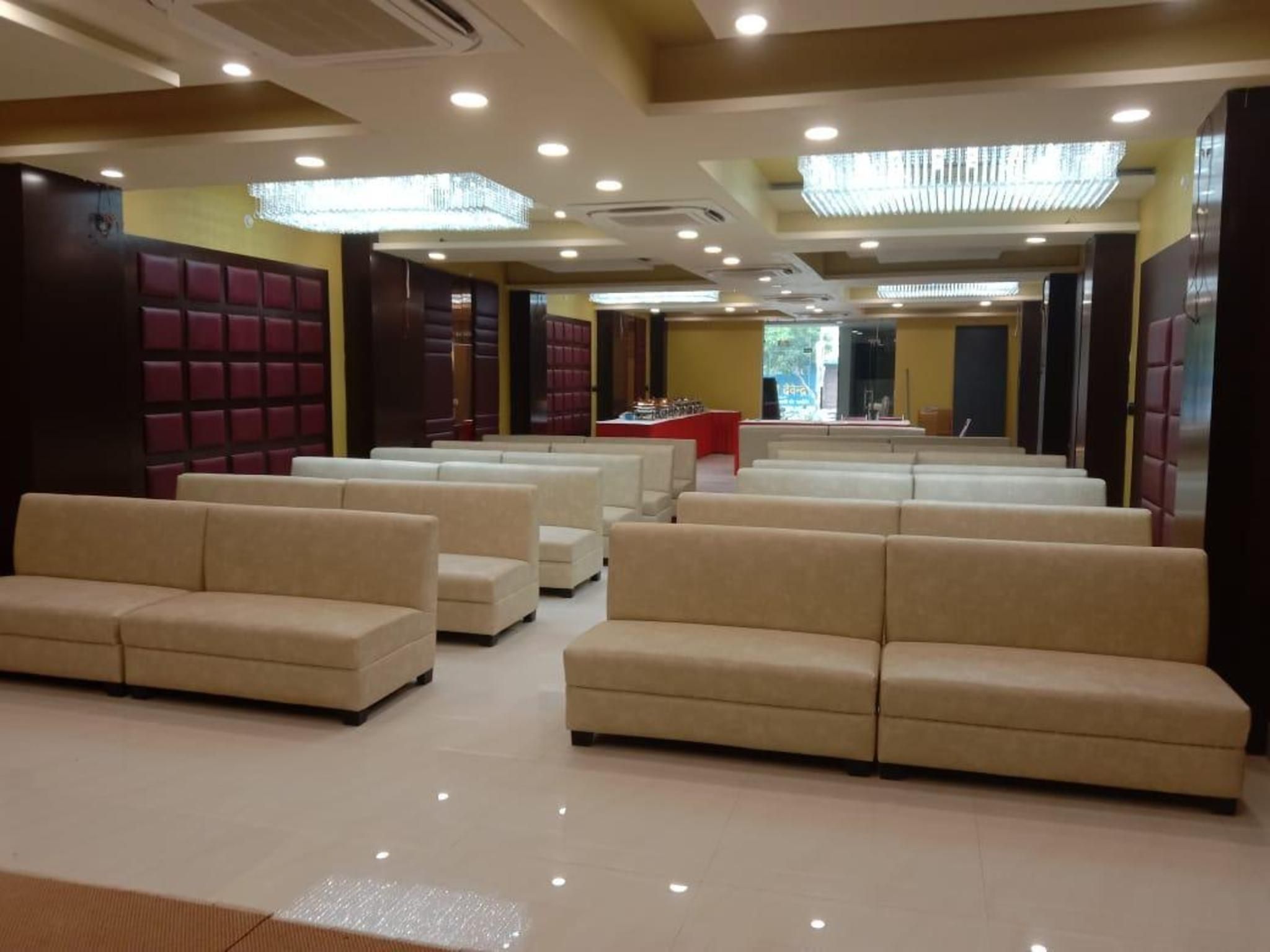 A hotel lobby with rows of beige sofas, a reception desk, and a chandelier.