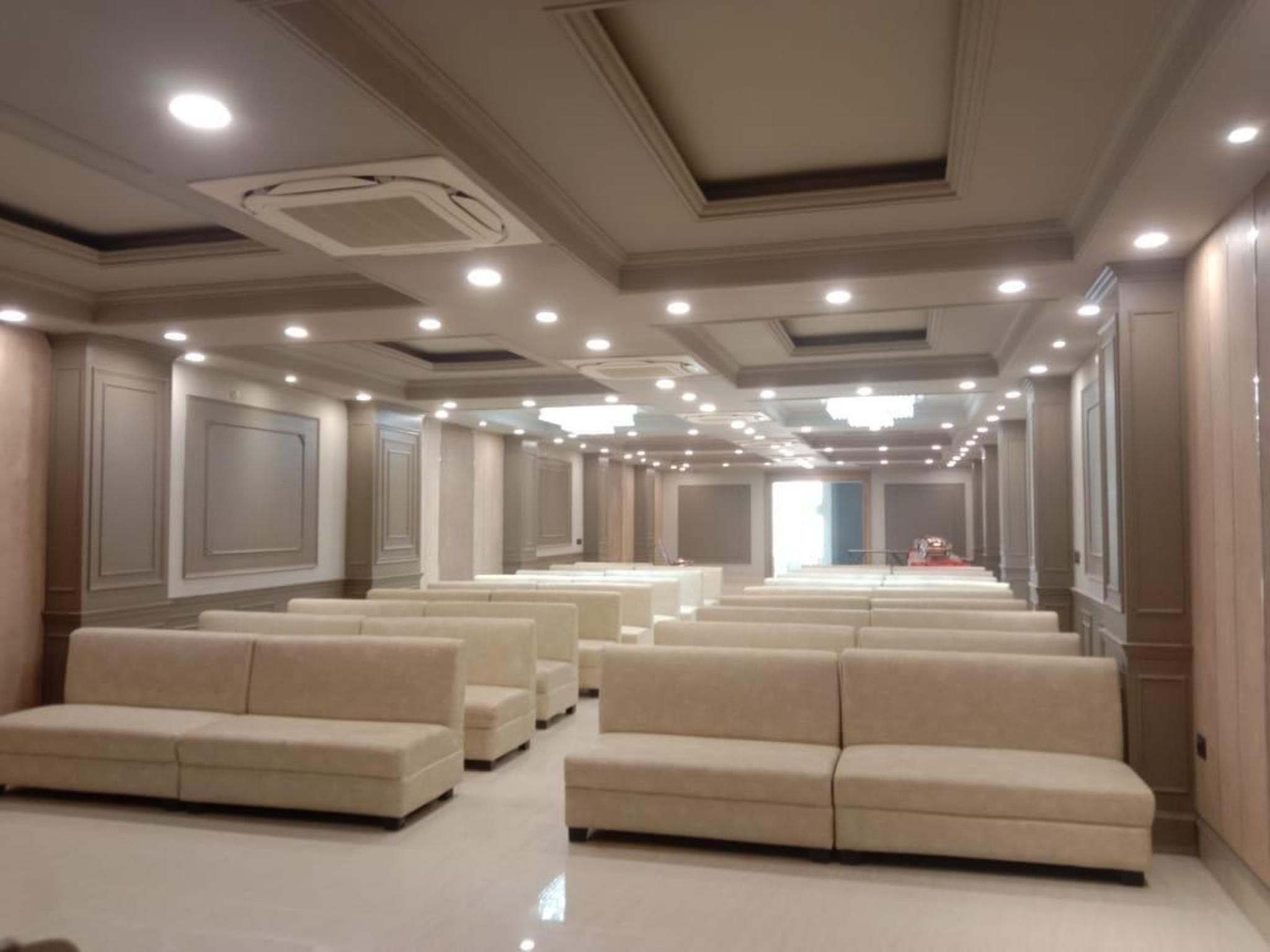 A hotel lobby with rows of beige sofas and a long corridor leading to a bright room.