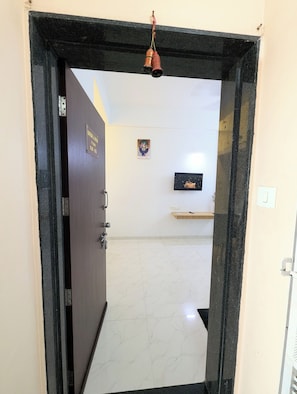 A doorway with a black frame, a small hanging bell, a door with a sign, a wall-mounted picture, and a shelf with a small item.
