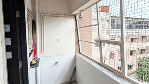 Ein schmaler Balkon mit Fliesenboden, einer Tür, einem Fenster mit Metallgitter und Blick auf benachbarte Gebäude.