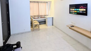 Ein Zimmer mit Deckenventilator, Wand-Fernseher, Bett mit Kopfkissen und Schreibtisch mit Stuhl.