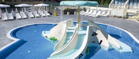 A pool with a water slide and lounge chairs.