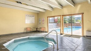Piscina interior com placa de posto de salva-vidas, mesa com cadeiras e vista para a área da piscina exterior.