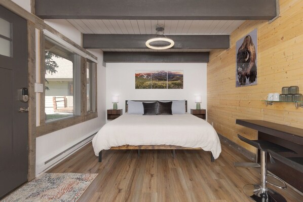 A bedroom with a bed, a desk, a chair, a window, and artwork on the wall.