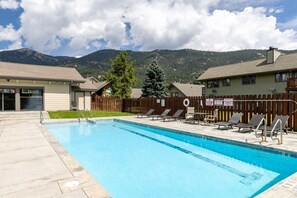 A swimming pool with lounge chairs, a wooden fence, and a mountain backdrop.