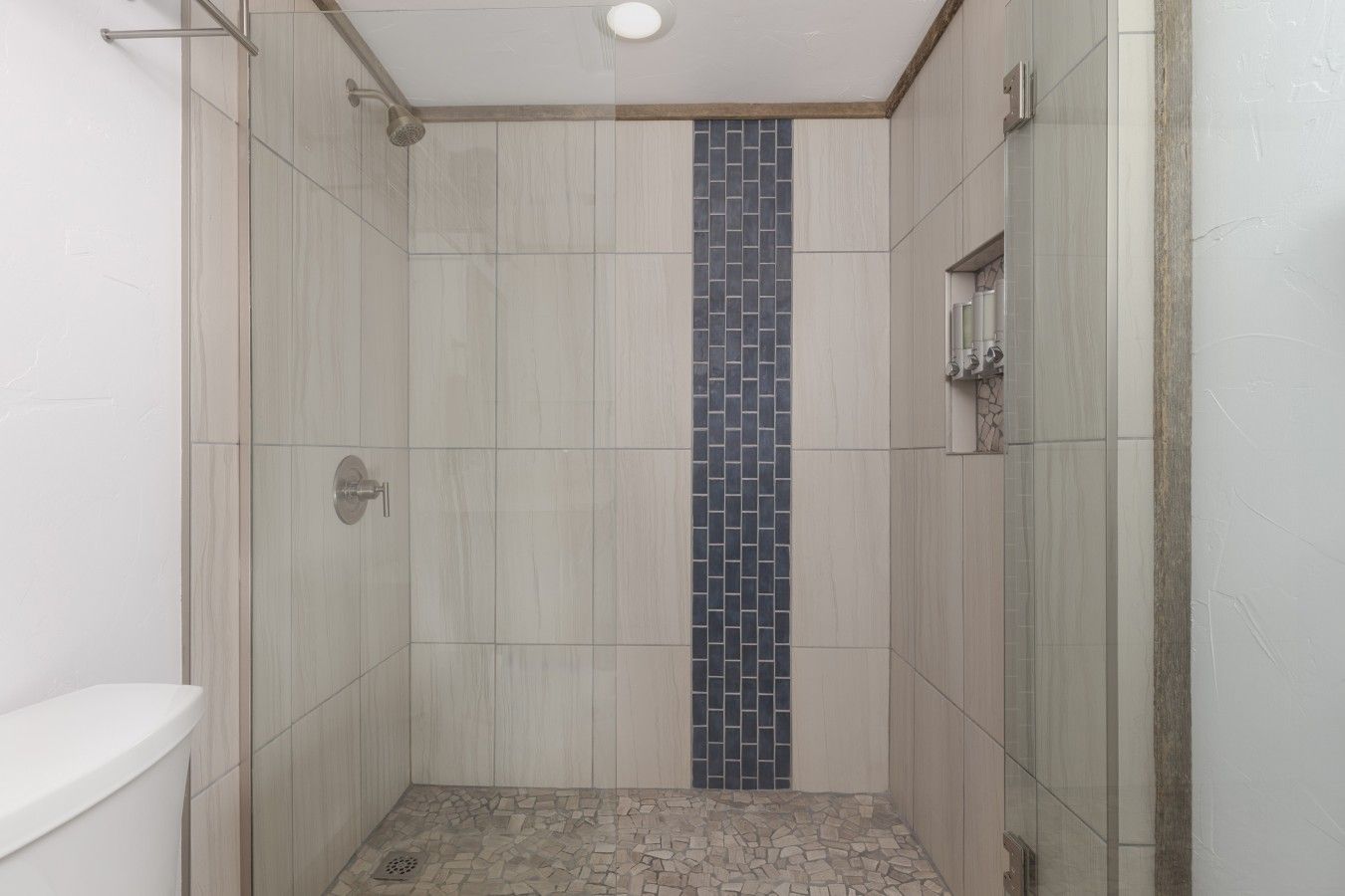 Een douche met een verticale tegelaccent, een douchekop en een betegelde vloer.